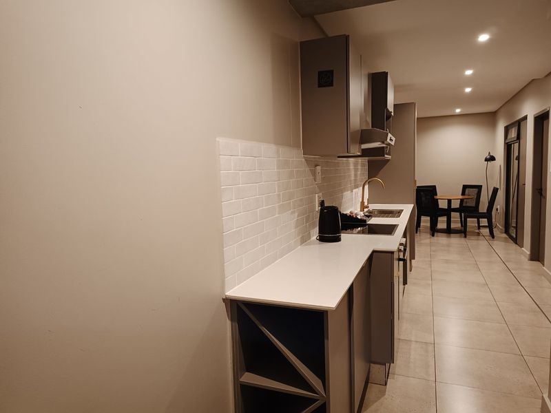 Modern kitchen featuring sleek cabinetry, subway tile backsplash, brass fixtures, and integrated wine storage, flowing into an open-plan dining area.