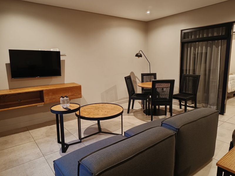A modern open-plan living and dining area featuring tiled floors, recessed lighting, and a wall-mounted media console with access to an outdoor space.