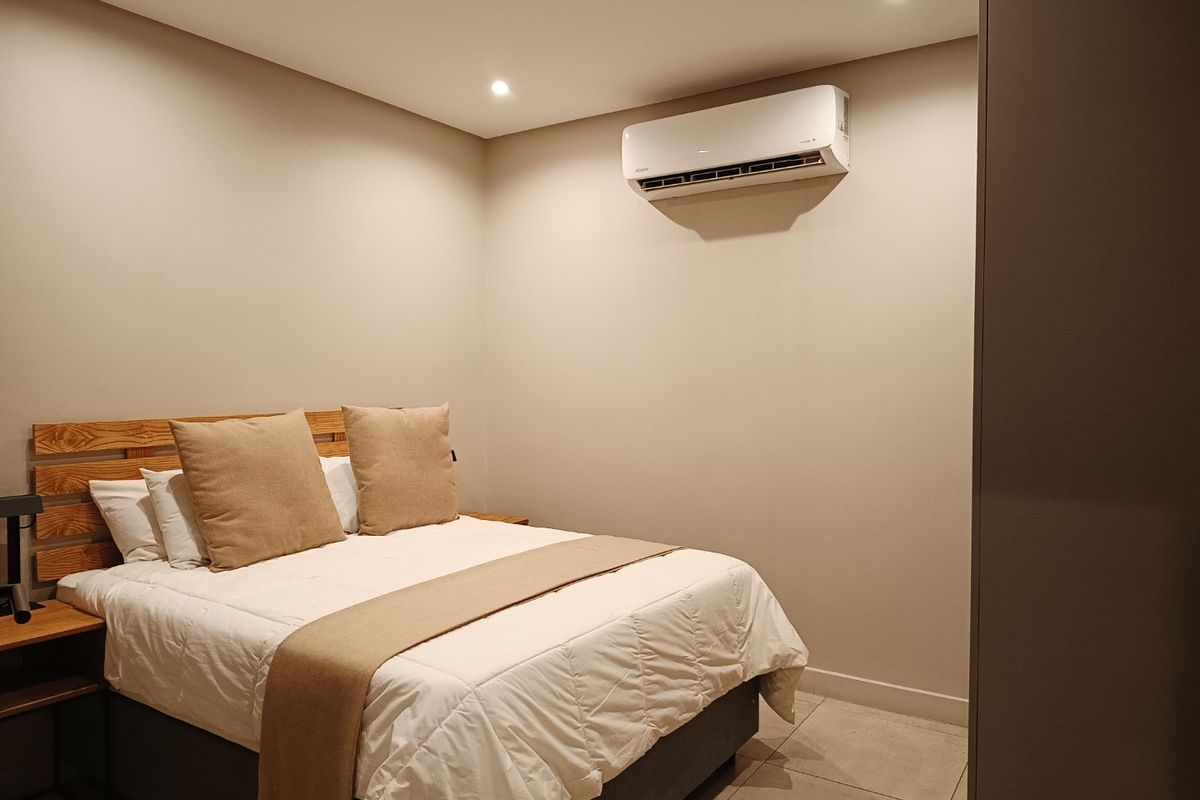 A modern, well-maintained bedroom featuring tiled flooring, recessed downlighting, and a wall-mounted split-system air conditioning unit.