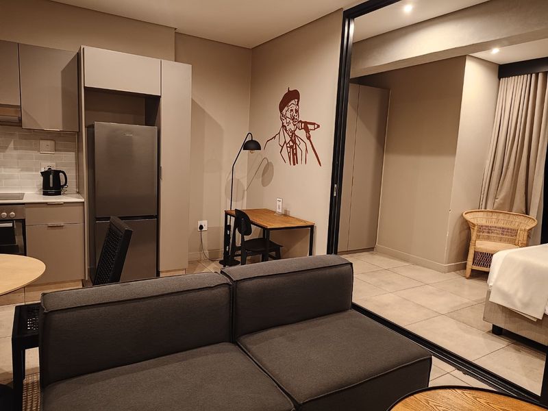Modern open-plan apartment featuring a compact kitchen with built-in cabinetry, tiled flooring, and a sliding glass partition separating the living and sleeping areas.