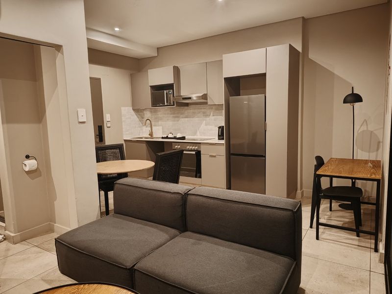 Modern open-plan apartment featuring a compact kitchen with built-in appliances, tiled flooring, and recessed lighting, seamlessly integrated with the living and dining area.