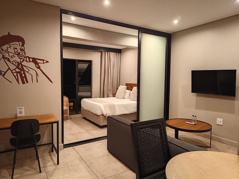 Modern open-plan apartment featuring a bedroom separated by a sleek sliding glass partition, tiled floors, and contemporary recessed lighting.