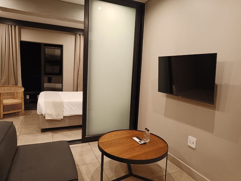 Modern open-plan living area featuring tiled flooring, a sleek sliding glass partition, and neutral wall finishes, seamlessly connecting to the bedroom space.