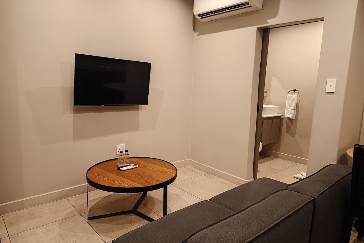 A modern living area featuring neutral wall tones, tiled flooring, and a wall-mounted air conditioning unit, with direct access to an adjoining bathroom.
