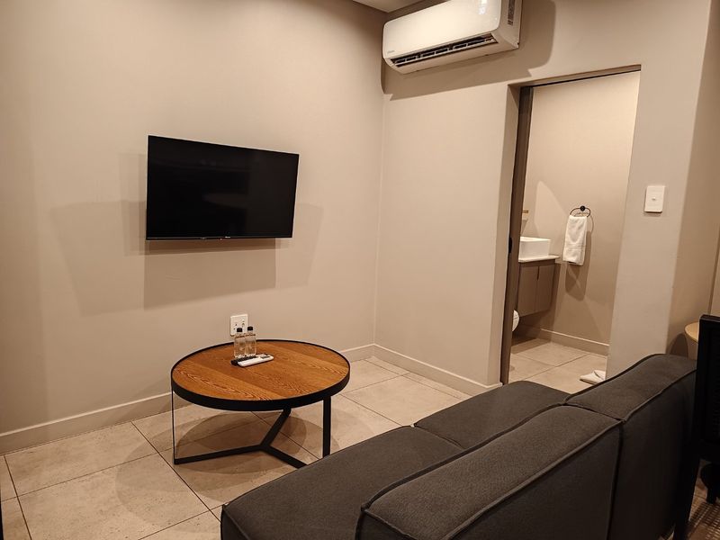 A modern living area featuring neutral wall tones, tiled flooring, and a wall-mounted air conditioning unit, with direct access to an adjoining bathroom.