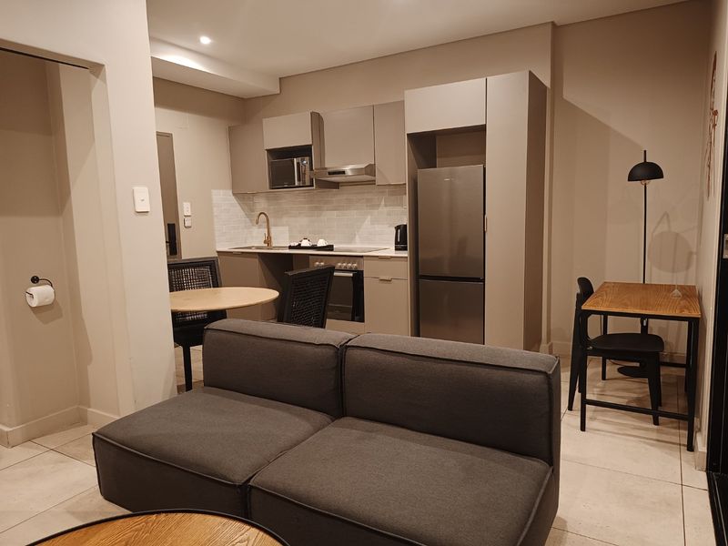 Modern open-plan living area featuring a compact, well-equipped kitchen with built-in cabinetry, integrated appliances, and neutral tiled flooring throughout.