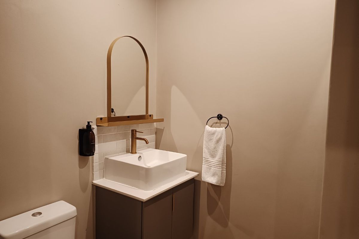 A modern bathroom featuring a vanity cabinet with a vessel sink, brass faucet, arched mirror, and subway tile backsplash.