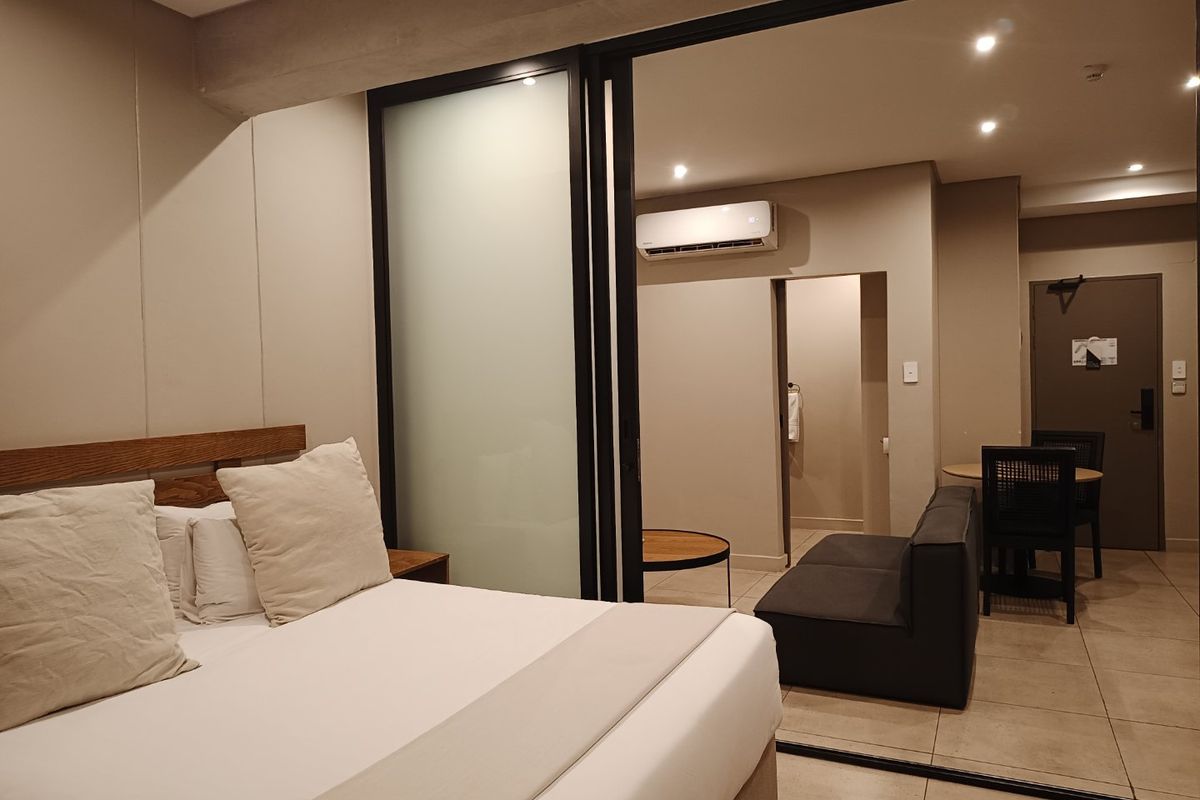 A modern bedroom featuring a sliding glass partition, tiled flooring, recessed lighting, and a wall-mounted split-system air conditioner.