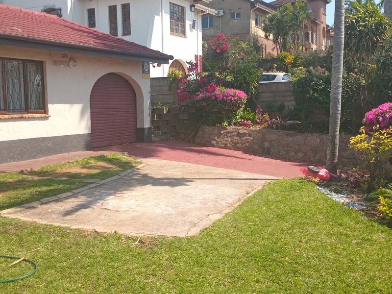 Front exterior view of the house featuring a tiled roof, garage access, and a concrete driveway set within a landscaped garden area.