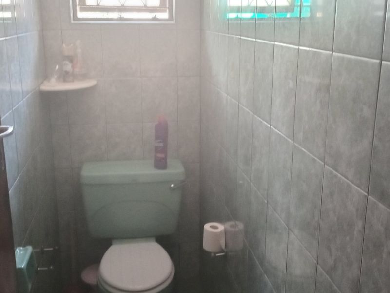 A compact bathroom featuring full-height ceramic wall tiling, a standard toilet, and a small window with security bars.