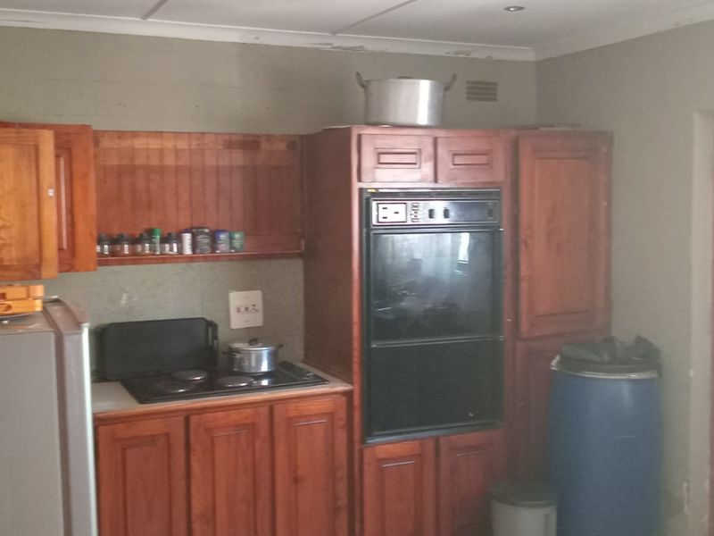 A dated kitchen featuring traditional wooden cabinetry, a built-in oven, and an electric hob, requiring cosmetic updates to modernize the space.