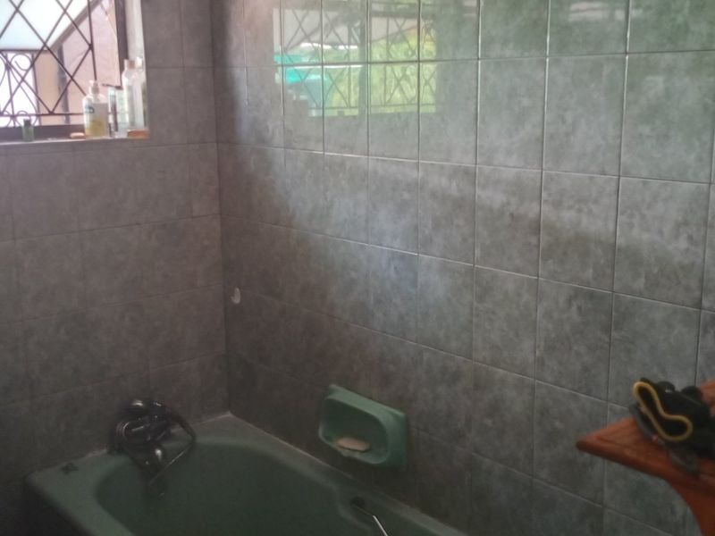 A dated bathroom featuring green sanitary ware, tiled walls, and a window with security bars.