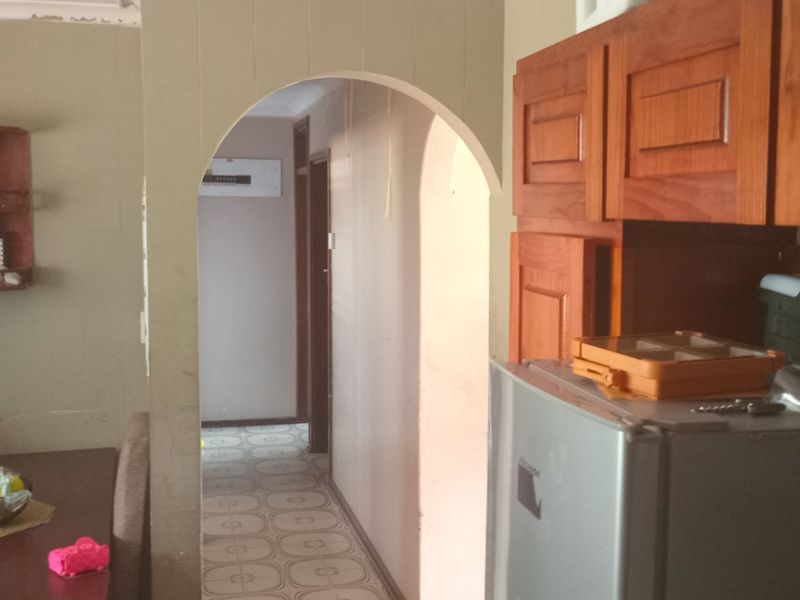 A dated kitchen area featuring wooden cabinetry and a classic archway leading to a hallway with tiled flooring.