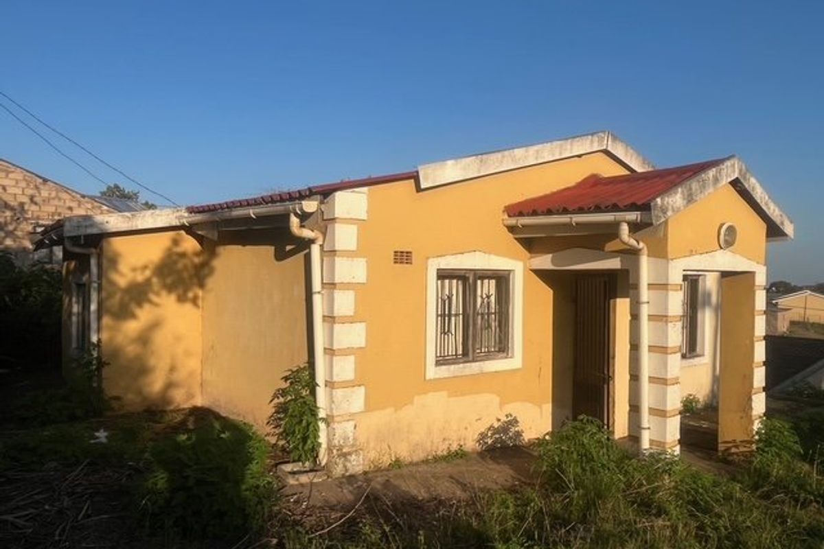 A detached single-story house featuring a yellow facade with white corner detailing, metal security bars on windows, and a tiled roof.