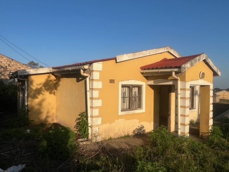 A detached single-story house featuring a yellow facade with white corner detailing, metal security bars on windows, and a tiled roof.