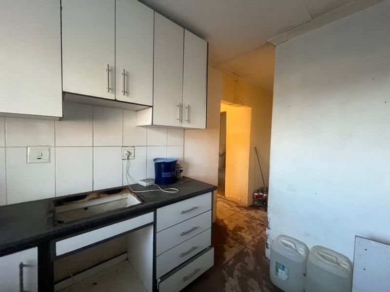 A dated kitchen area featuring built-in cabinetry and tiled backsplash, currently requiring significant renovation and repair to the countertop and flooring.
