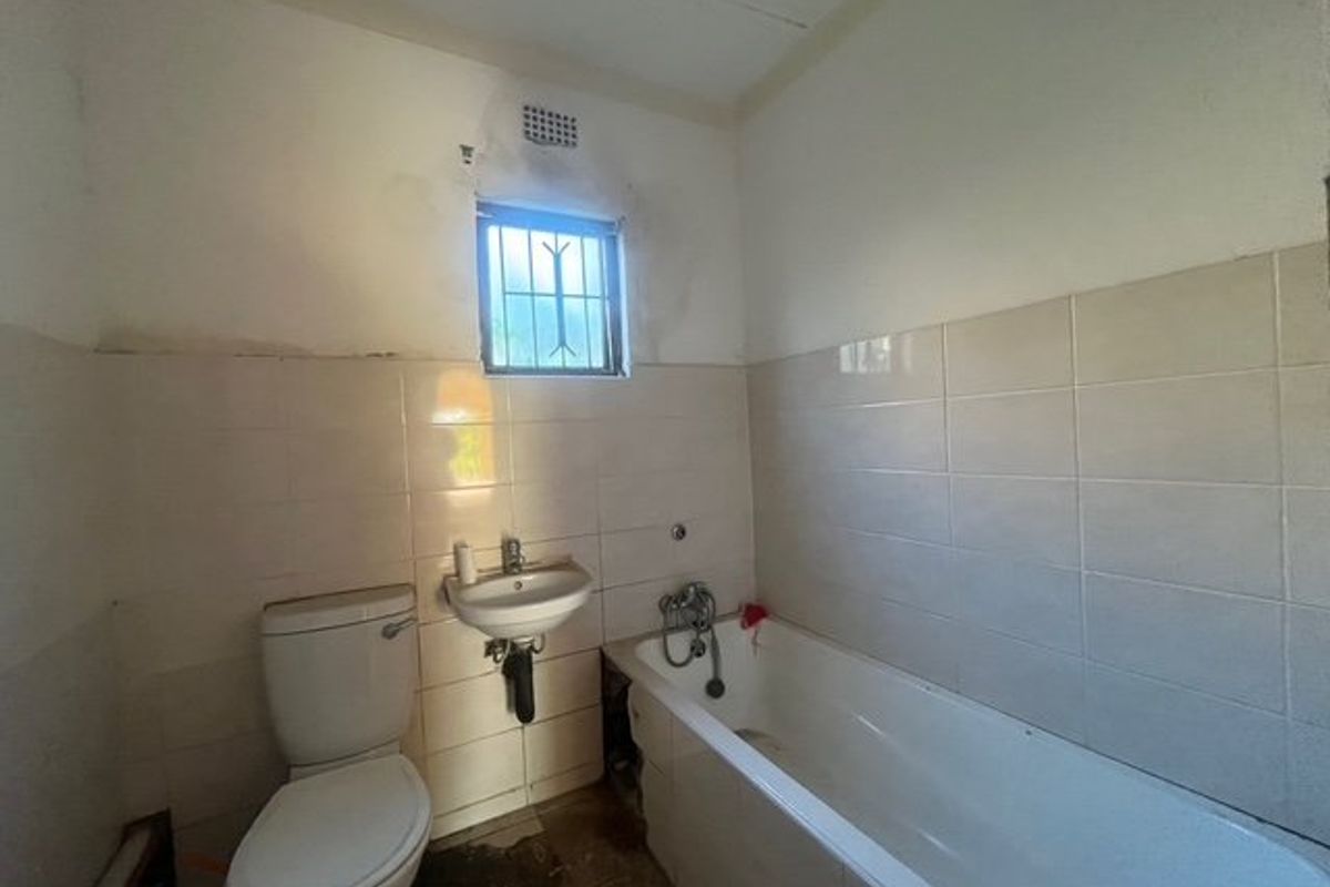 A dated bathroom featuring a standard bathtub, wall-mounted basin, and toilet, requiring renovation and repair to the ceiling and wall finishes.