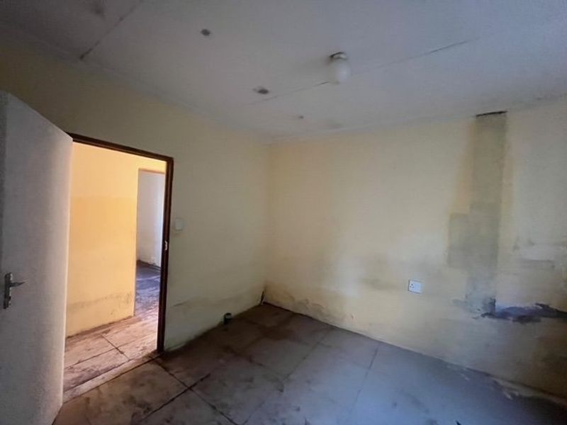 An empty bedroom featuring tiled flooring and visible wall damage, requiring renovation and cosmetic updates to restore the space.