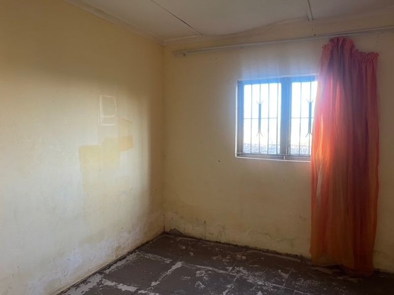 An empty bedroom featuring security bars on the window and tiled flooring, requiring cosmetic updates and wall repairs.