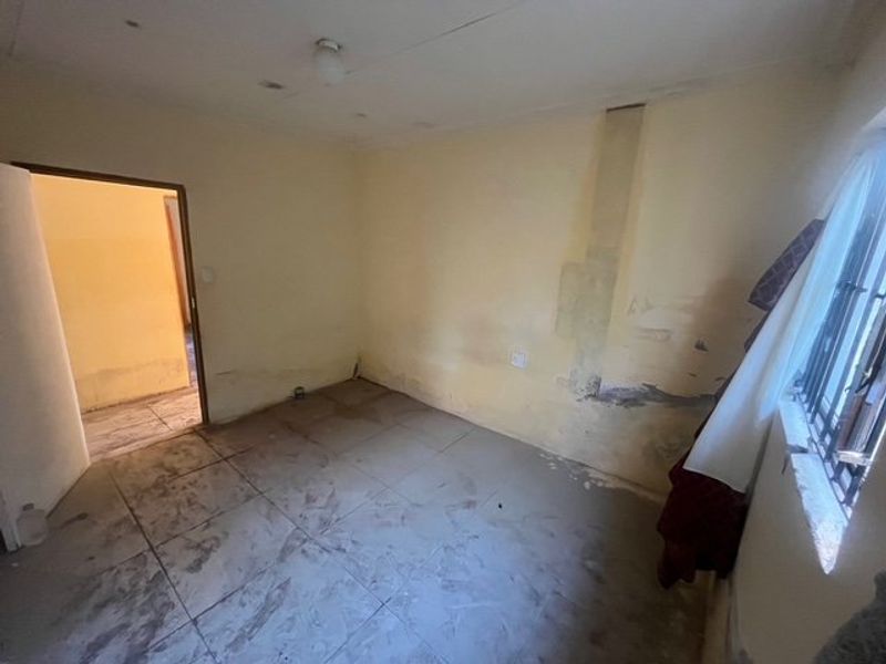 An empty bedroom featuring tiled flooring and security bars on the window, currently requiring significant wall repairs and cosmetic refurbishment.