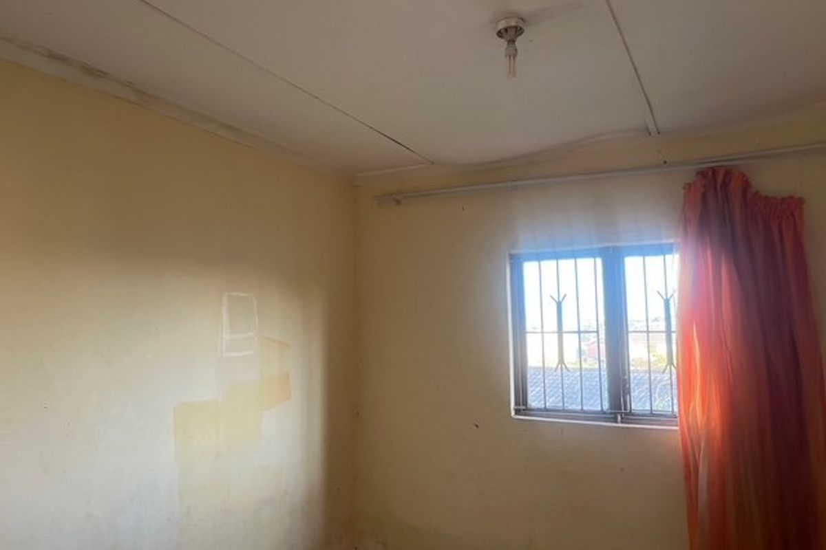 An empty bedroom featuring security bars on the window and a basic ceiling light fixture, requiring cosmetic updates and wall repairs.