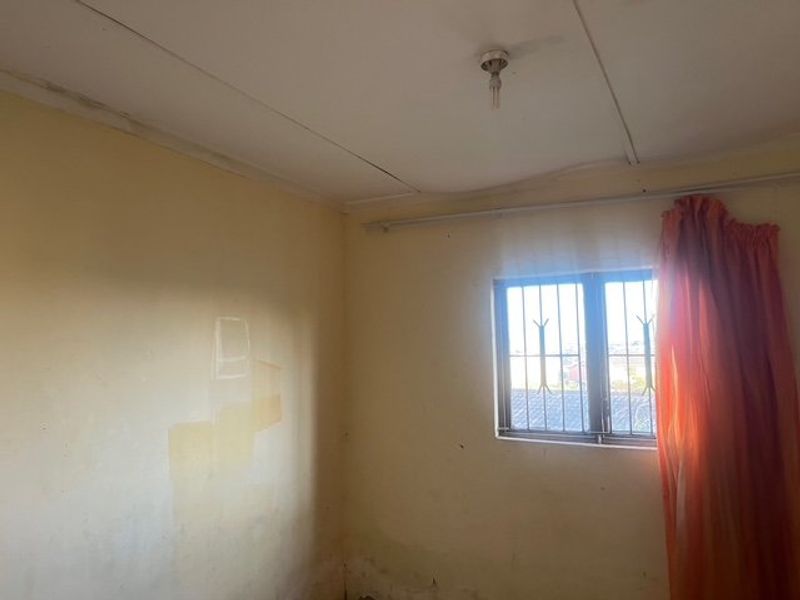 An empty bedroom featuring security bars on the window and a basic ceiling light fixture, requiring cosmetic updates and wall repairs.