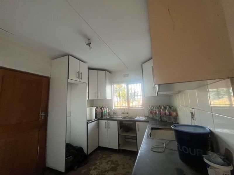 A compact kitchen featuring built-in cabinetry, a double sink, and tiled splashbacks, currently requiring significant maintenance and cosmetic updates.