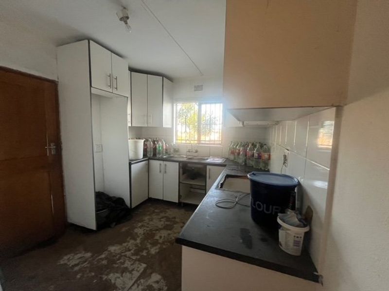 A dated kitchen featuring white built-in cabinetry, laminate countertops, and a tiled backsplash, requiring significant renovation and flooring repairs.