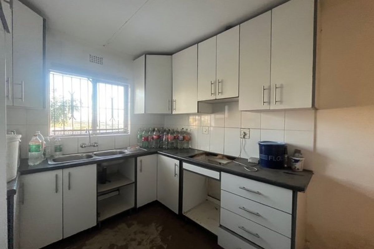 A functional kitchen featuring white cabinetry, laminate countertops, and a double basin sink, currently requiring updates to flooring and missing appliance integration.