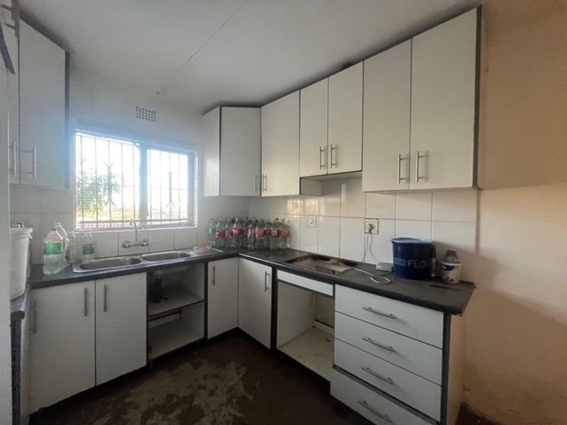 A functional kitchen featuring white cabinetry, laminate countertops, and a double basin sink, currently requiring updates to flooring and missing appliance integration.