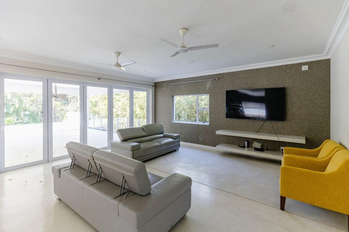 Spacious living room featuring a textured accent wall, built-in floating shelving, dual ceiling fans, and large sliding glass doors opening to the outdoors.