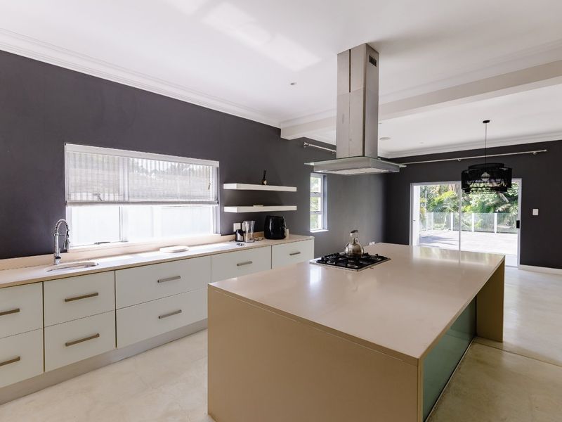 Modern kitchen featuring a large central island with gas hob, sleek cabinetry, stone countertops, and direct access to the outdoor patio area.
