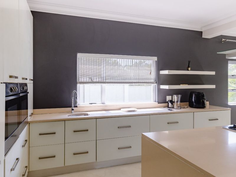 Modern kitchen featuring sleek white cabinetry, stone countertops, built-in oven, gas hob, and floating shelves against a dark accent wall.