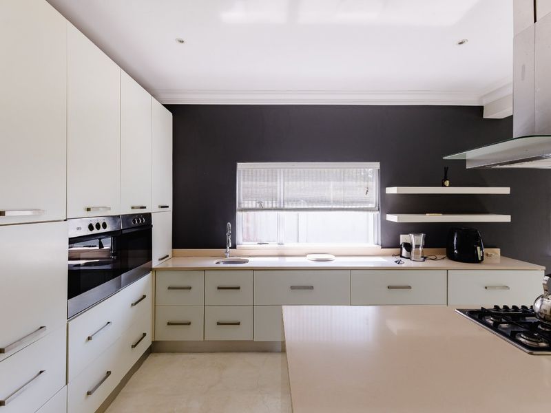 Modern kitchen featuring white cabinetry, stone countertops, built-in oven, gas hob, and a sleek extractor fan against a dark feature wall.