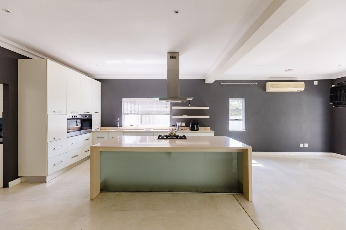 Modern open-plan kitchen featuring a central island with gas cooktop, built-in oven, sleek cabinetry, and polished concrete floors in a neutral color palette.