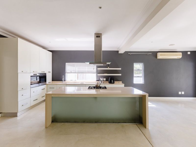 Modern open-plan kitchen featuring a central island with gas cooktop, built-in oven, sleek cabinetry, and polished concrete floors in a neutral color palette.