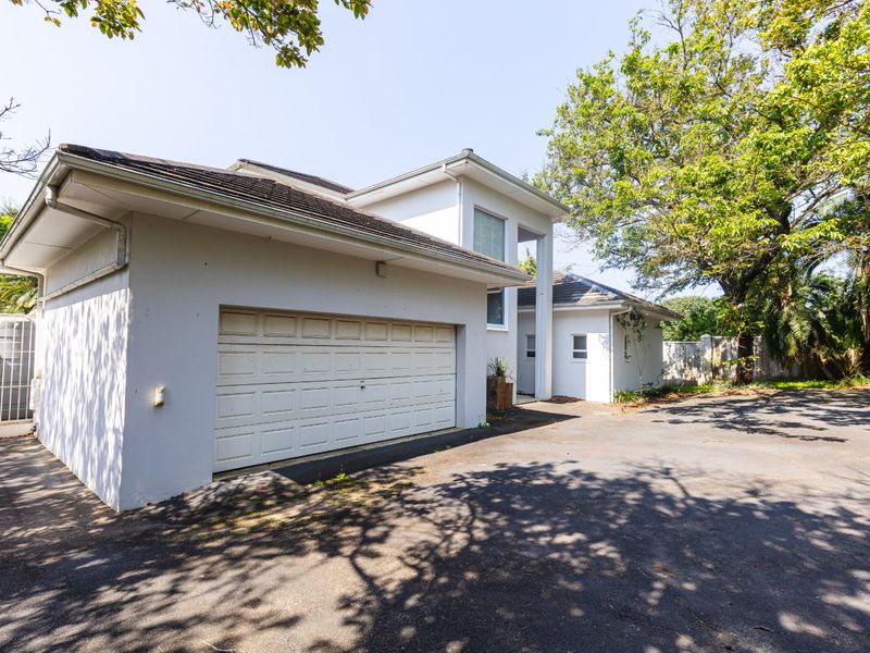 Front exterior view of the property featuring a double garage, paved driveway, and established surrounding trees.