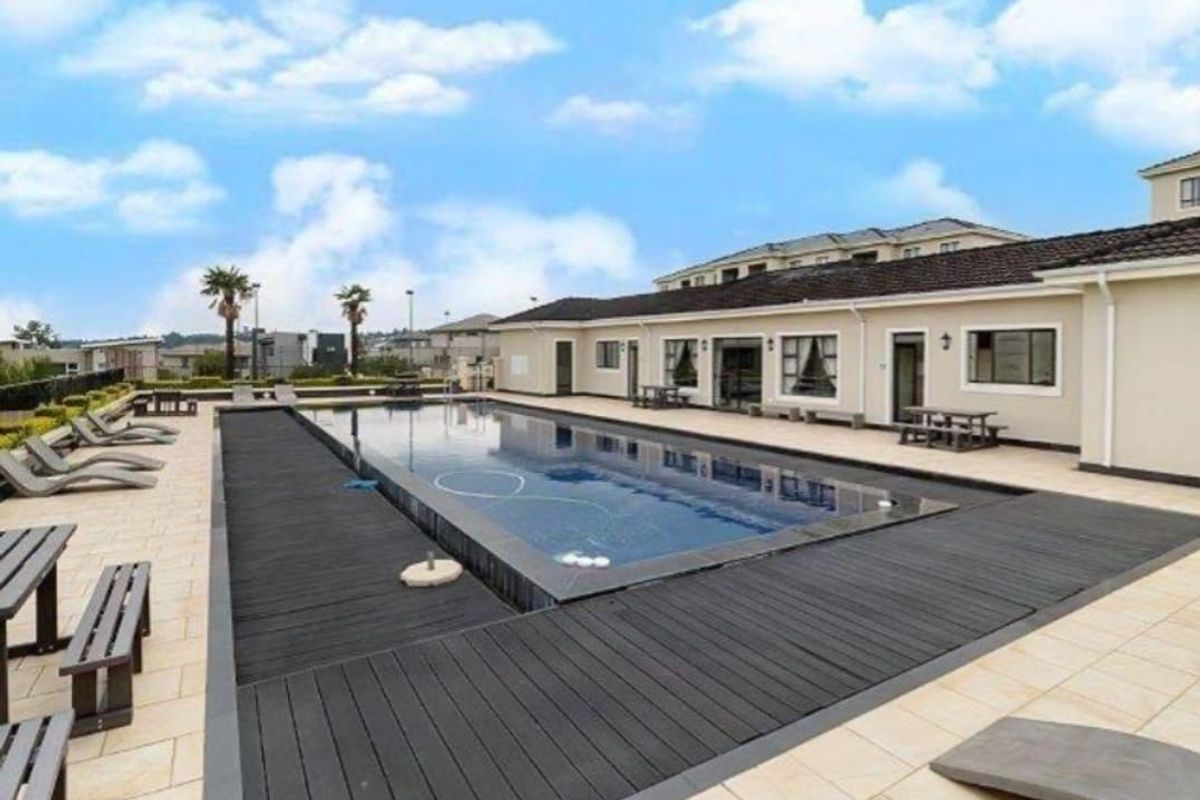 A well-maintained communal swimming pool area featuring modern timber decking, tiled surround, and direct access to the apartment building exterior.
