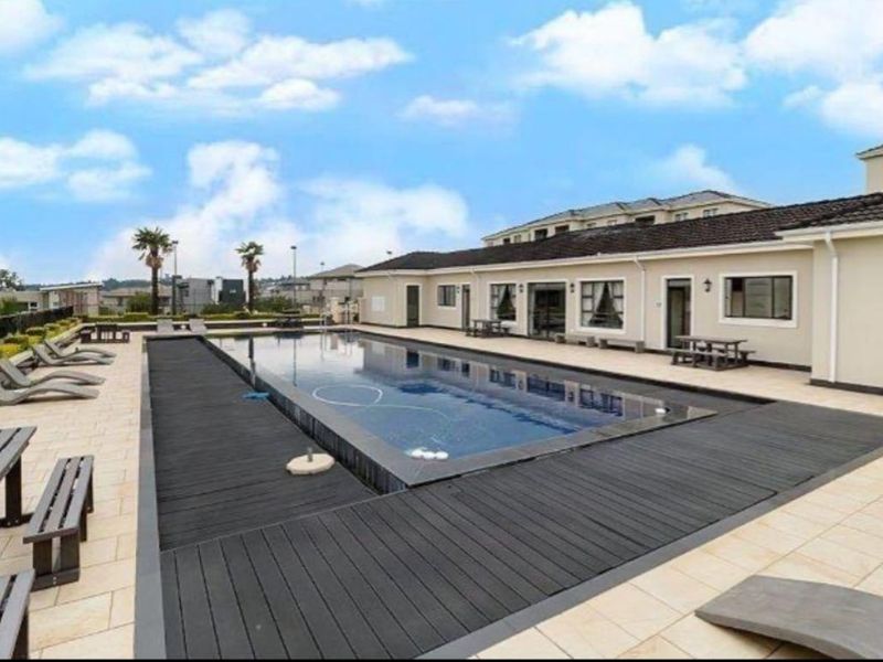 A well-maintained communal swimming pool area featuring modern timber decking, tiled surround, and direct access to the apartment building exterior.