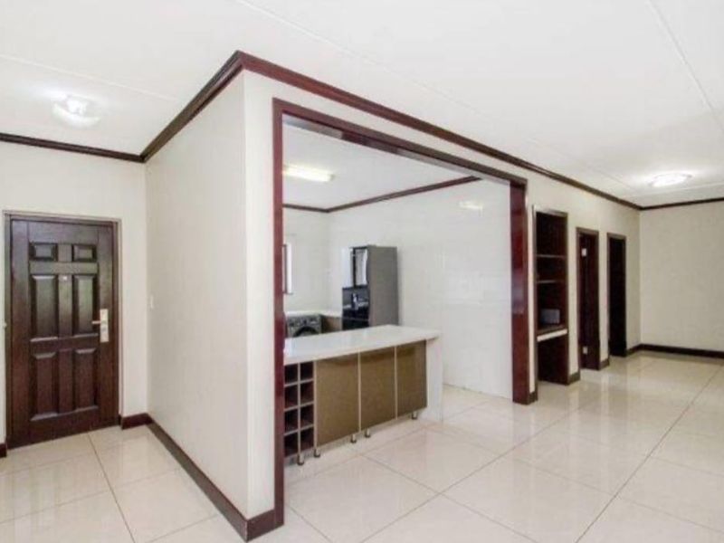 Open plan living area featuring tiled flooring, built-in kitchen cabinetry with a breakfast bar, and integrated shelving units.