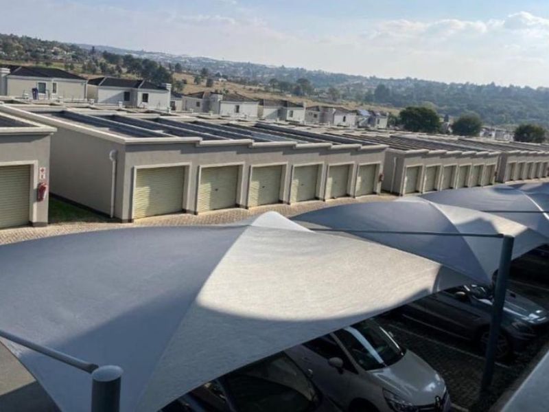 Elevated view of a residential complex featuring a row of garages with roller shutter doors and covered shade cloth parking bays.