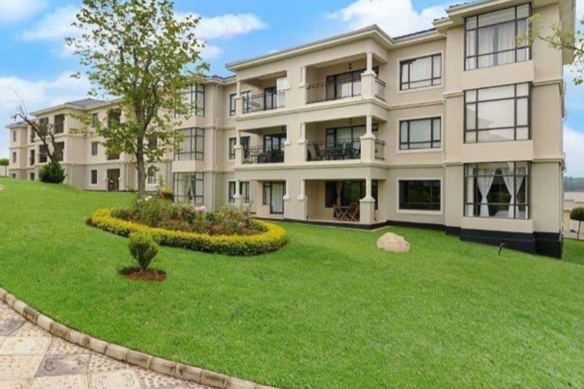 A view of the rear apartment building facade featuring multiple balconies, large windows, and a well-maintained landscaped garden area.