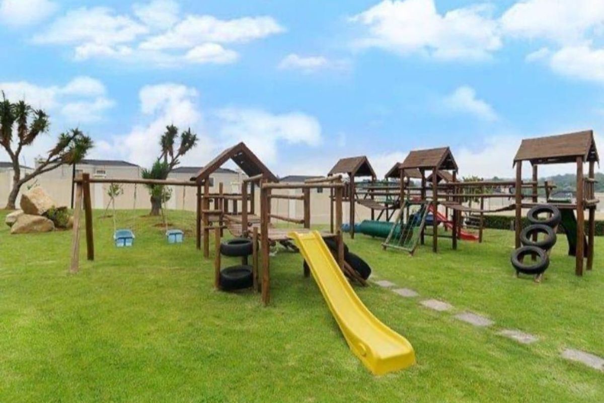A well-maintained communal garden area featuring a wooden playground structure with slides and swings set on a grassy lawn.