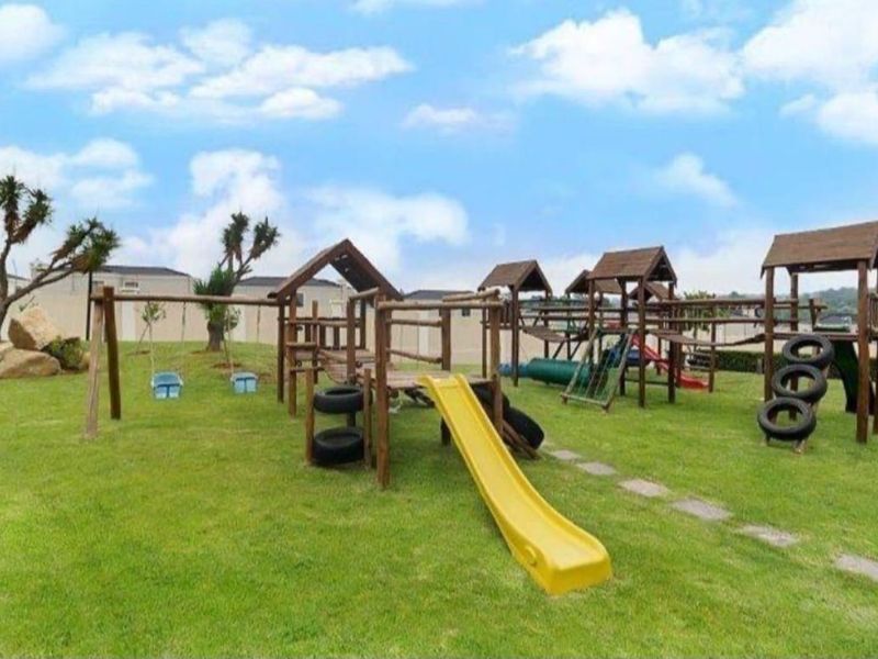 A well-maintained communal garden area featuring a wooden playground structure with slides and swings set on a grassy lawn.