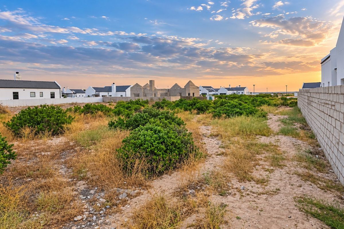 A view of a vacant residential plot featuring a boundary wall, set within a developing estate at sunset.
