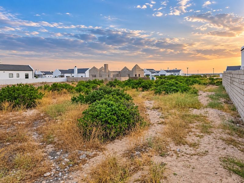 A view of a vacant residential plot featuring a boundary wall, set within a developing estate at sunset.