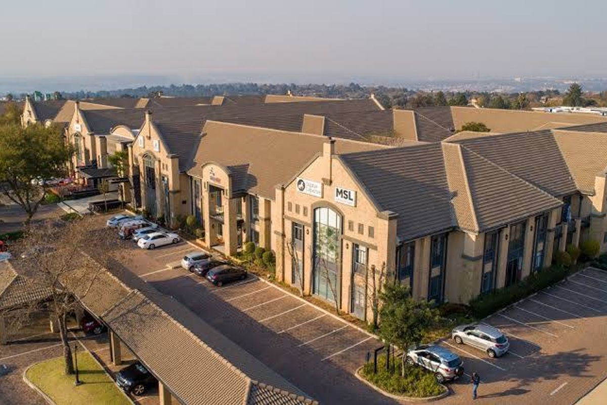 Aerial view of a commercial office complex featuring tiled roofing, extensive paved parking, and covered parking bays.