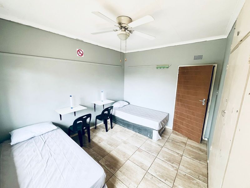 A functional bedroom featuring tiled flooring, a ceiling fan, and built-in wall-mounted desks, providing a practical space for rest and study.