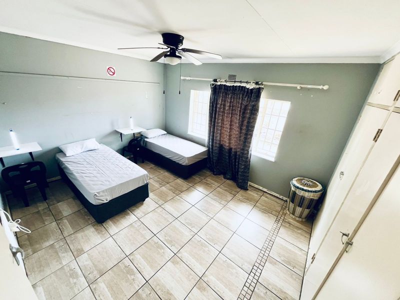 A functional bedroom featuring tiled flooring, a ceiling fan, and built-in cupboards, providing a practical living space.