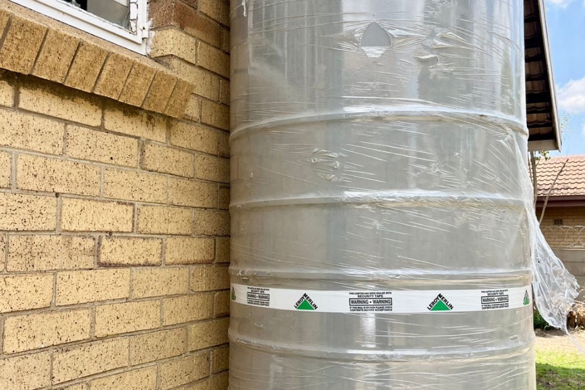 A vertical water storage tank installed against the exterior brick wall of the house.